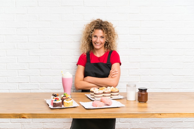 Mujer joven con muchos mini pasteles diferentes en una mesa riendo