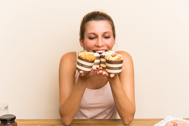 Mujer joven con muchos mini pasteles diferentes en una mesa