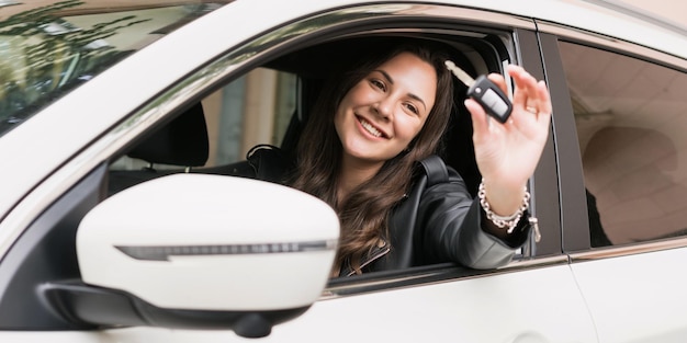 Una mujer joven muestra las llaves de un auto nuevo Compra costosa de un auto moderno