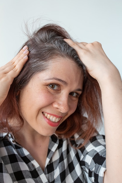 Mujer joven muestra sus raíces de cabello gris concepto de envejecimiento temprano