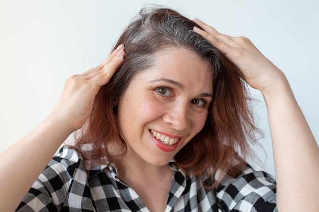 Mujer joven muestra sus raíces de cabello gris concepto de envejecimiento temprano