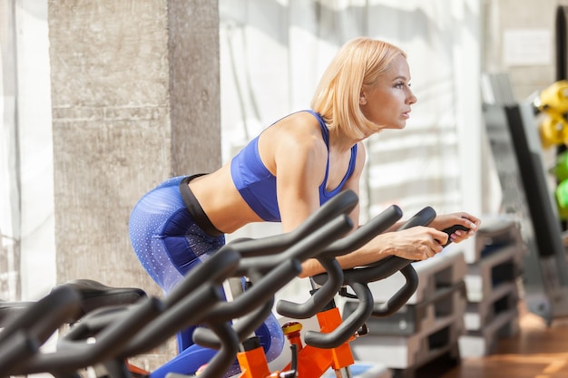 Mujer joven muscular en bicicleta en el gimnasio entrenamiento cardiovascular intenso