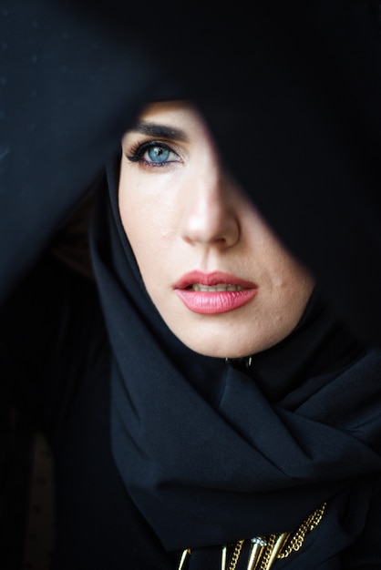 Mujer joven musulmana sobre fondo oscuro con hijab negro