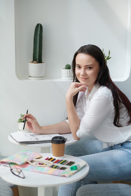 Foto mujer joven muy sonriente pasar tiempo haciendo dibujos en el cuaderno de bocetos con lápices de colores y bolígrafos de tinta