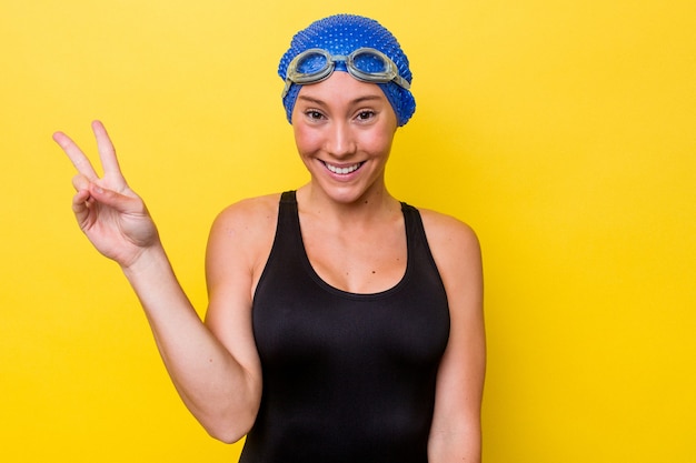 Mujer joven nadador australiano aislada sobre fondo amarillo que muestra el signo de la victoria y una amplia sonrisa.