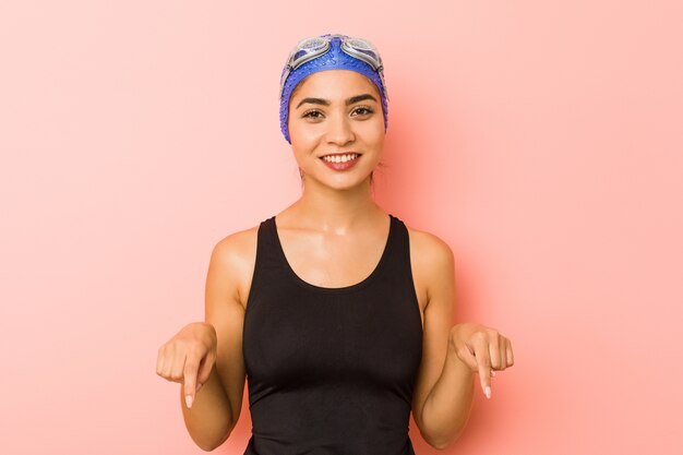 Mujer joven nadadora árabe aislada apunta hacia abajo con los dedos, sentimiento positivo.