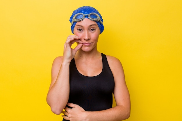 Mujer joven nadadora australiana aislada sobre fondo amarillo con los dedos en los labios guardando un secreto.