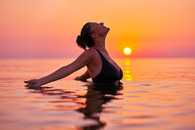 Mujer joven nadando en el mar al amanecer.