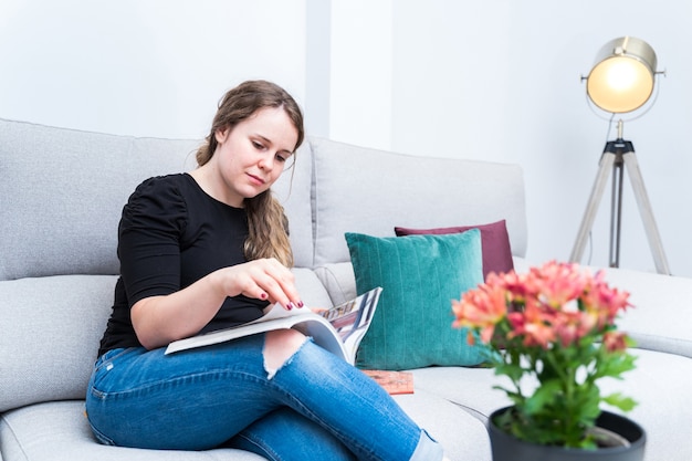 Mujer joven navegando por la revista de decoración en su sala de estar. reformas, estilo de vida e interiores.