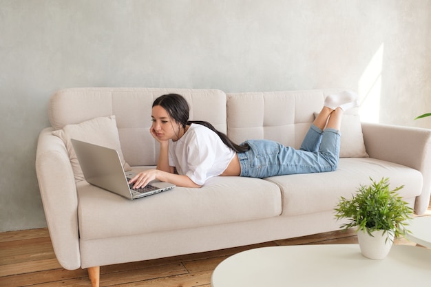 Mujer joven navegando en su computadora portátil en el sofá