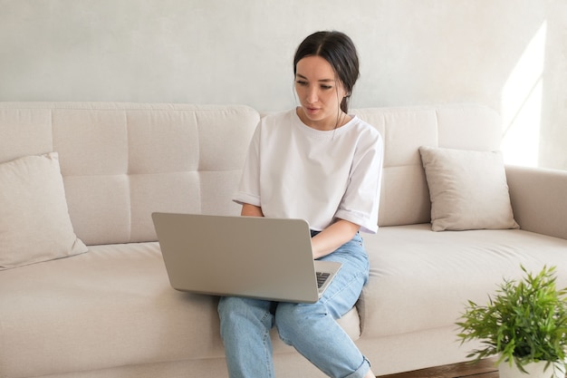 Foto mujer joven navegando en su computadora portátil en el sofá