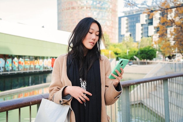 Mujer joven de negocios asiática seria viendo en la aplicación de teléfono celular un mensaje de texto al aire libre Niña china infeliz leyendo noticias en el teléfono inteligente