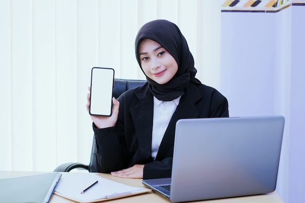 Mujer joven de negocios feliz sosteniendo un teléfono móvil en la oficina