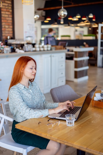 Mujer joven de negocios se sienta en las mesas de un café y trabaja en una computadora portátil