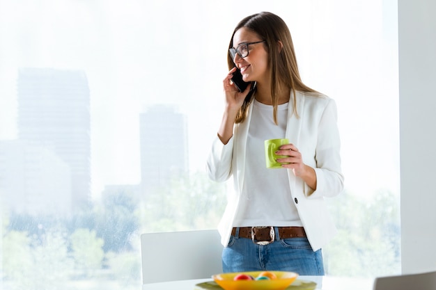 Mujer joven de negocios usando su teléfono móvil en la oficina.