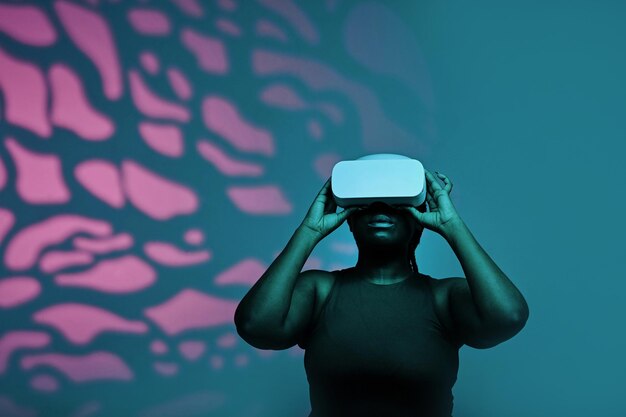 Mujer joven negra con gafas inalámbricas viendo la realidad virtual contra el fondo rosa