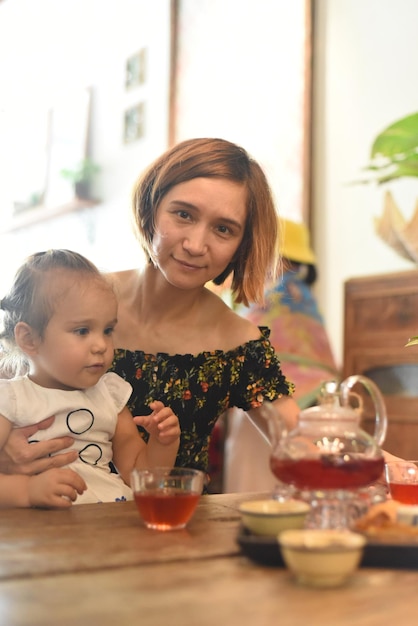 Mujer joven con una niña bebiendo té de una tetera en una cafetería.