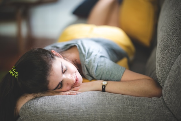 Mujer joven niña bonita que vive y descansa en paz en un acogedor sofá, sofá disfrutando, tumbado, relajarse en la habitación del apartamento interior, sonreír comodidad