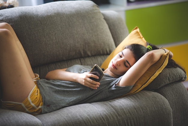 Mujer joven niña bonita que vive y descansa en paz en el acogedor sofá, sofá disfrutando, tumbado, relajarse en la habitación del apartamento interior, sonrisa de comodidad