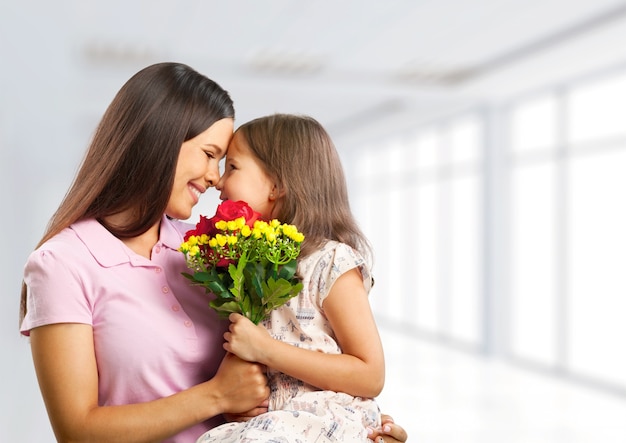 Mujer joven con niña y hermosas flores en la habitación