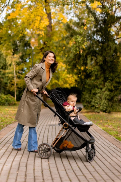 Foto mujer joven con una niña linda en un cochecito en el parque de otoño