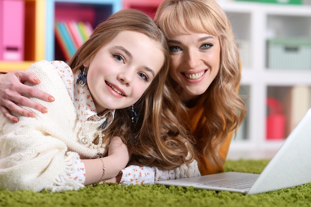 Foto mujer joven, con, niña, usar la computadora portátil, en casa, en, piso