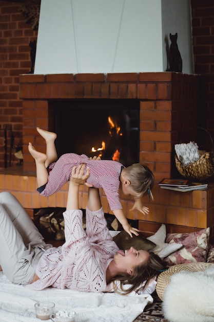 Mujer joven con un niño. Mamá e hijo están jugando, divirtiéndose cerca de la chimenea.