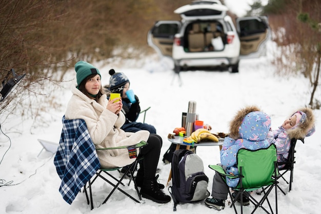 Mujer joven con niños en el bosque de invierno en un picnic Madre y tres hijos