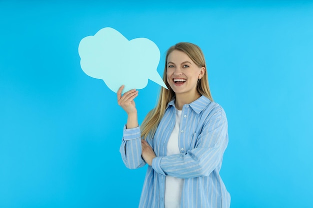 Mujer joven y nube de habla sobre fondo azul.