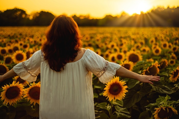 Mujer joven o niña disfrutando de la hermosa puesta de sol y los rayos del sol en el campo de los girasoles