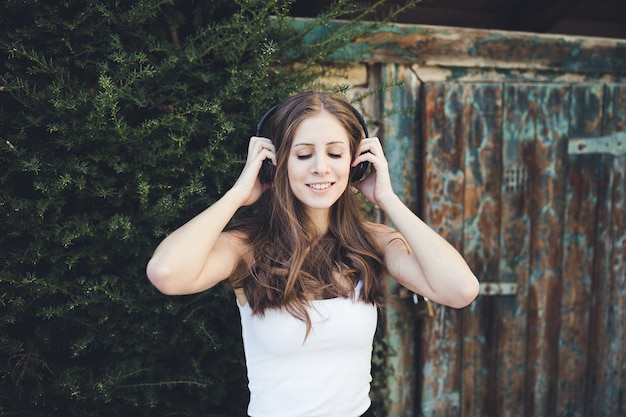 Mujer joven con los ojos cerrados escuchando música a través de auriculares al aire libre