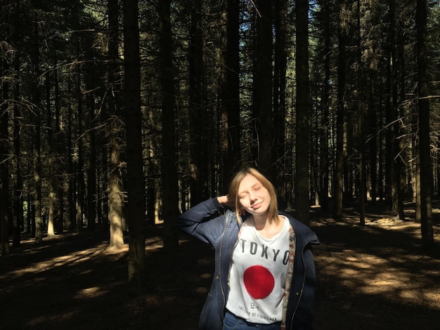 Foto mujer joven con los ojos cerrados de pie en el bosque