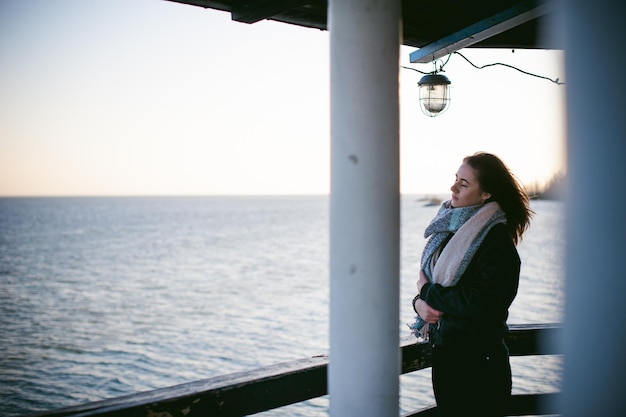 Foto mujer joven con los ojos cerrados de pie en el muelle sobre el mar contra un cielo despejado