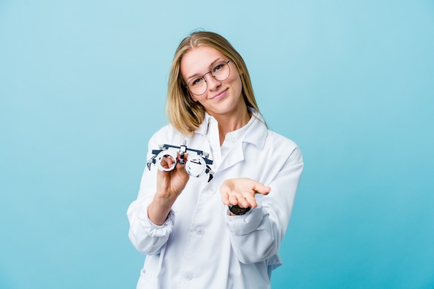 Mujer joven optometrista rusa en azul sosteniendo algo con las palmas
