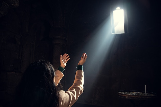 Mujer joven de oración a la luz de la iglesia.