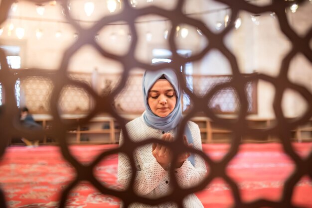 Foto mujer joven orando en la mezquita vista a través de la valla de la ventana