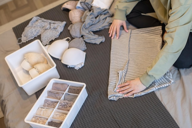 Mujer joven organizando el almacenamiento de ropa interior en el dormitorio contenedores plegados contemporáneos ropa