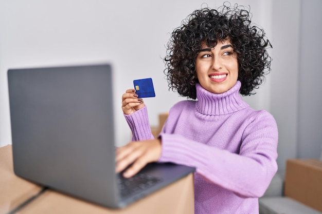 Mujer joven de oriente medio que usa una computadora portátil y una tarjeta de crédito en un nuevo hogar