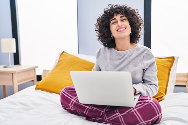 Mujer joven de Oriente Medio usando una computadora portátil sentada en la cama en el dormitorio