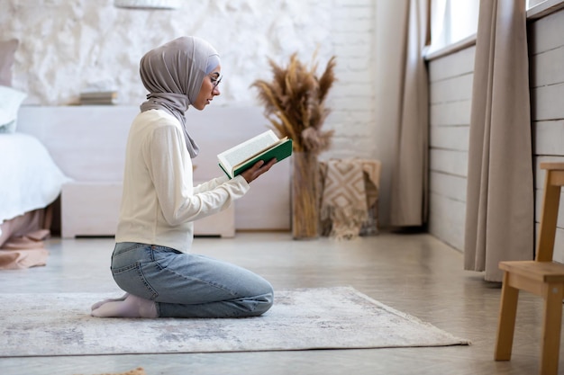 Una mujer joven de origen oriental y religión en un hiyab se sienta en casa de rodillas y con los brazos cruzados