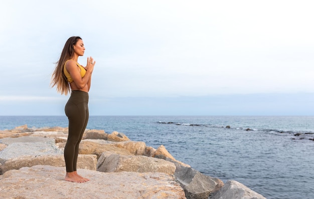 Mujer joven pacífica de pie junto al mar con las manos en oración. Copie el espacio. Concepto de espiritualidad y meditación.