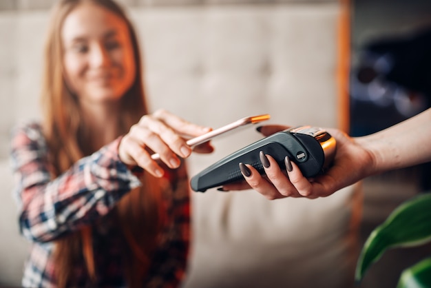 Mujer joven paga por teléfono móvil en la cafetería. Tecnologías de pago modernas