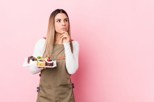 Mujer joven panadero con dulces mirando hacia los lados con expresión dudosa y escéptica.