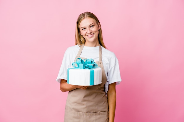 Mujer joven panadero ruso sosteniendo un delicioso pastel feliz, sonriente y alegre.