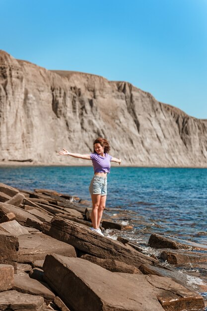 Una mujer joven en pantalones cortos en una playa rocosa de piedras naturales en Crimea