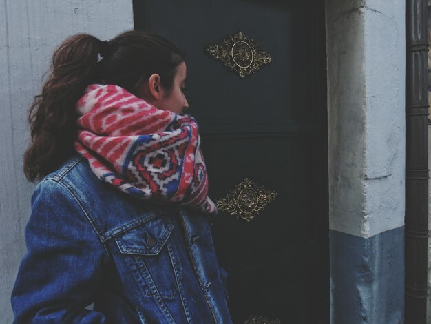 Foto mujer joven con pañuelo de pie junto a la puerta