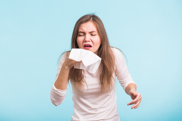 Mujer joven con pañuelo, tiene secreción nasal en la pared azul