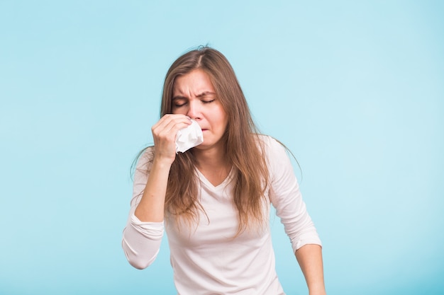 Mujer joven con pañuelo, tiene secreción nasal en la pared azul