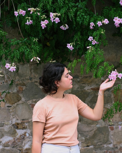 Foto mujer joven parada frente a una pared con flores en la mano