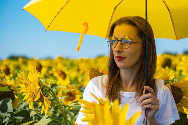 Mujer joven bajo el paraguas amarillo en el campo de girasol.